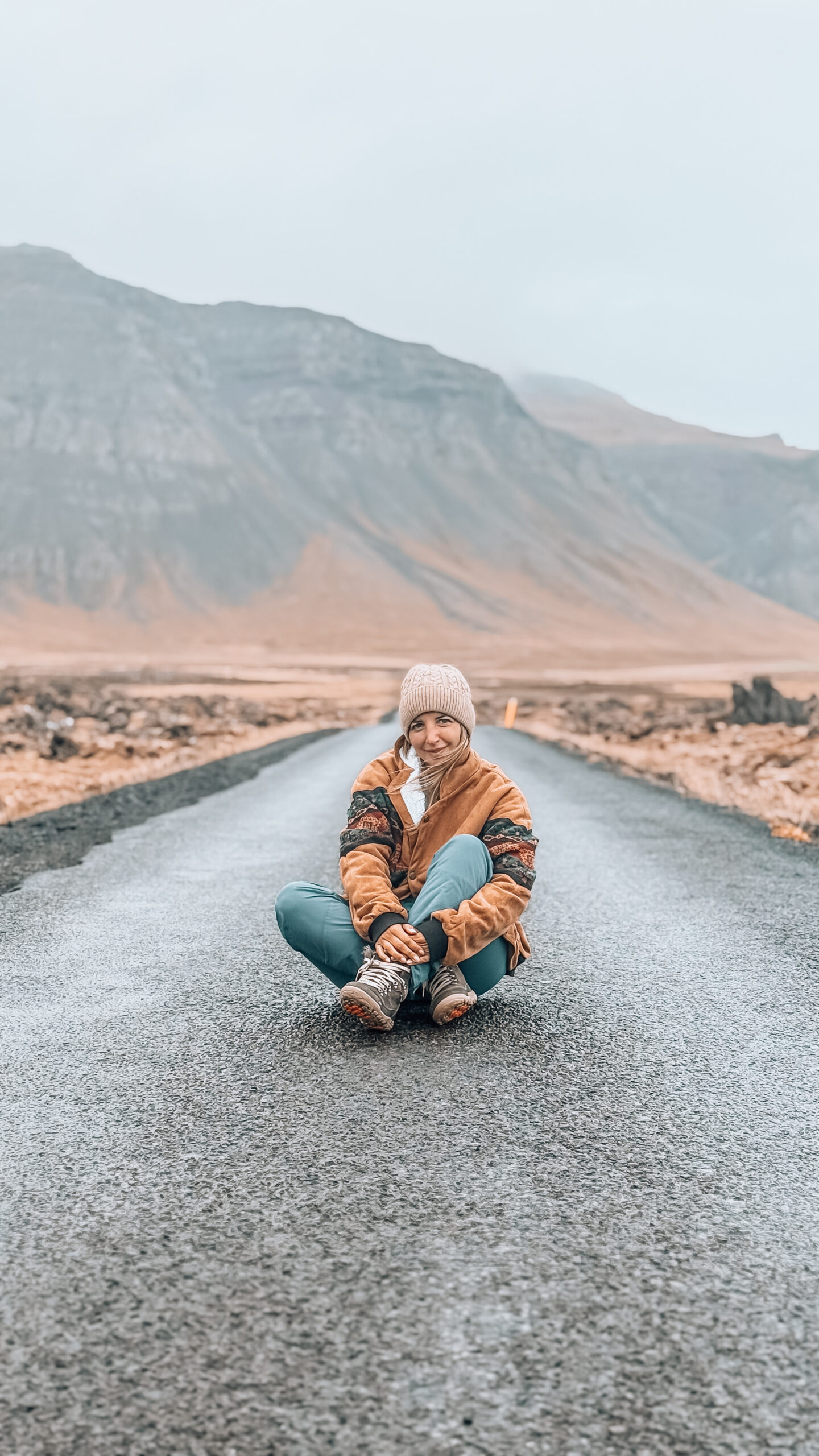 ragazza seduta nel mezzo di una strada islandese deserta in autunno