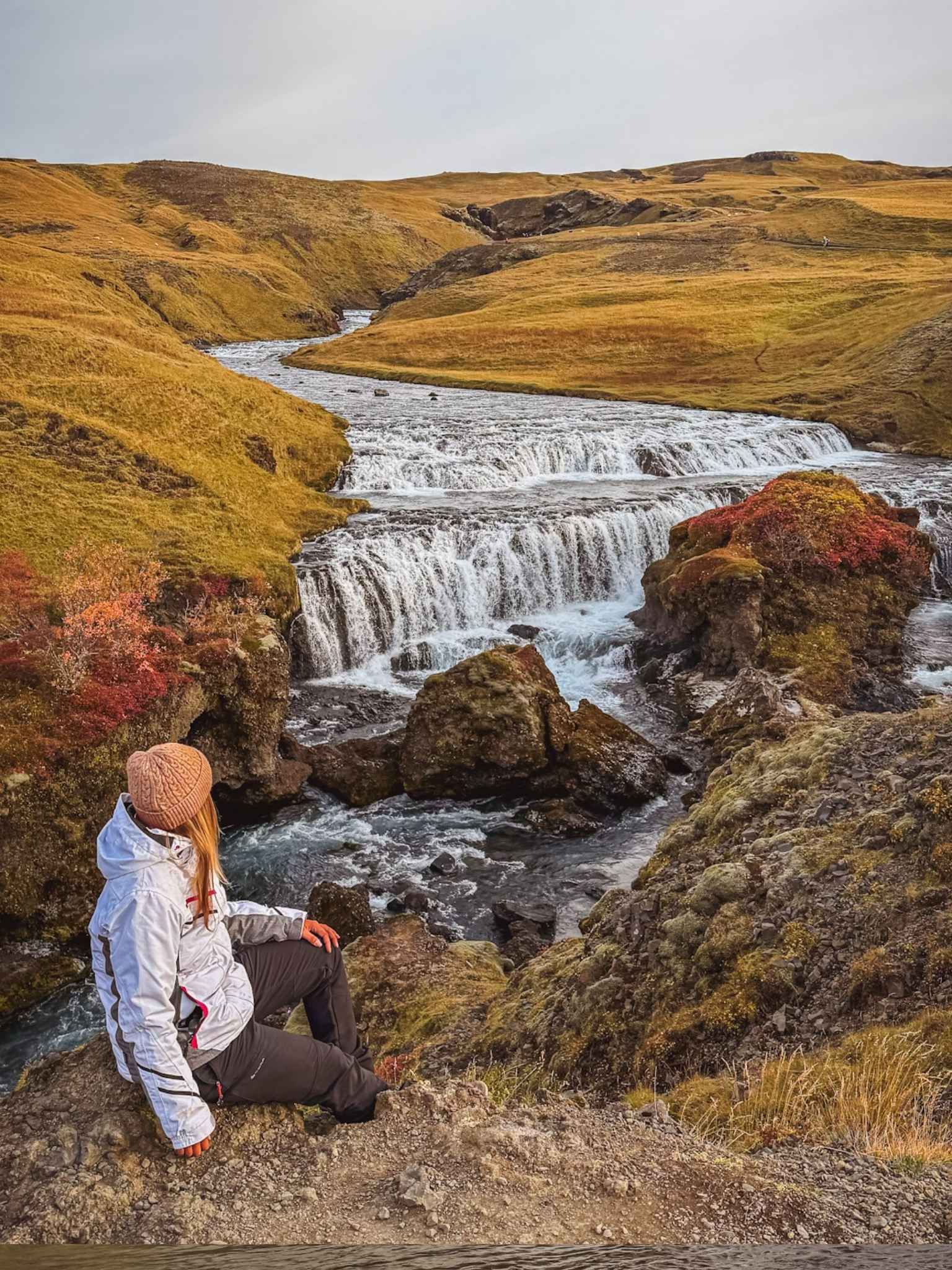 ragazza seduta su roccia che guarda cascata sul sentiero prima di Skogafoss